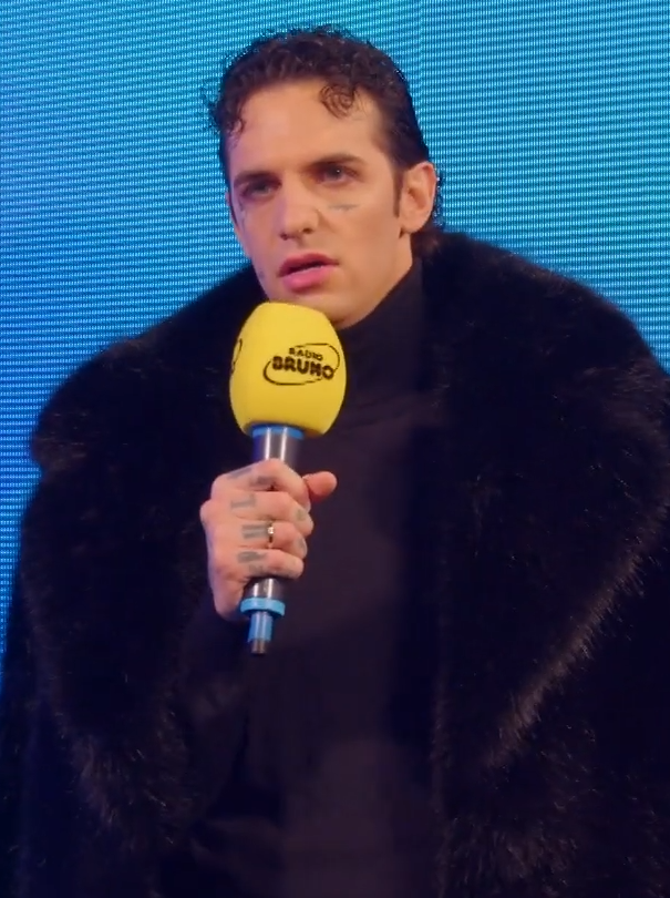 Achille Lauro durante un’intervista a Radio Bruno a Sanremo l’11 febbraio 2025, con cappotto nero e microfono giallo